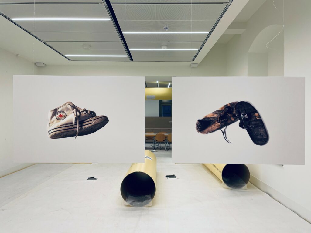 Blick in die Ausstellung. Zwei große Bilder von stark benutzen Schuhen hängen im Raum. 