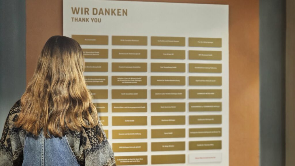 Besucherin betrachtet die Förderwand im Forum Wissen, auf der Spender*innen aufgeführt sind