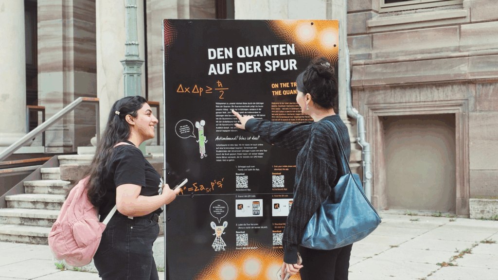 Zwei Frauen informieren sich an diener Stele über die interaktive Stadt-Rally zur Quanten-Ausstellung