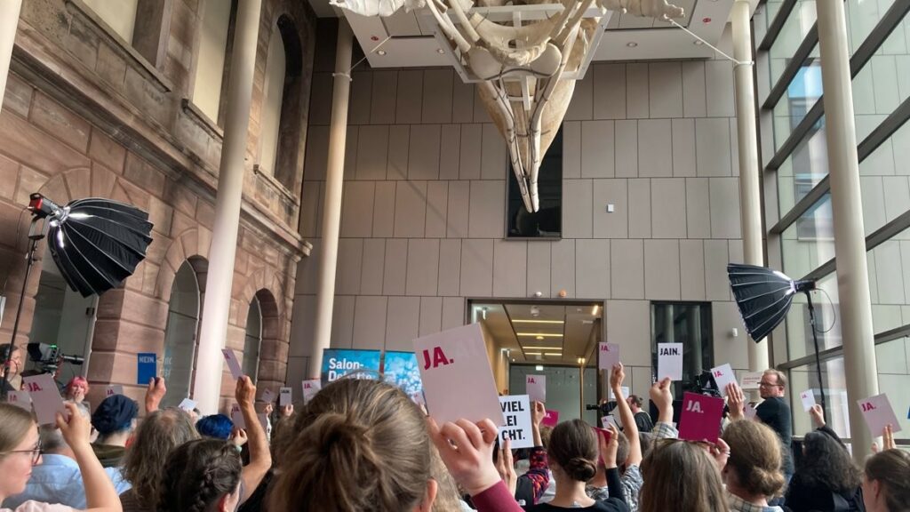 Publikum bei der Salondebatte im Forum Wissen, alle Leute stehen und halten Abstimmungskarten mit "Ja", "Nein" oder "Jein" in die Höhe