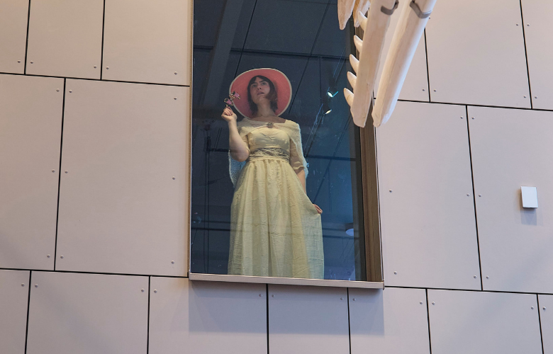 Die Kommunikatorin Pelin Öszu als Dorothea Schlözer, mit einem Kleid und Hut passend zum 18. Jahrhundert. Vom ersten Stock schaut sie hinunter auf das Café im Forum Wissen