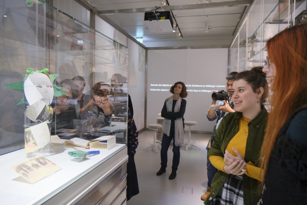 Besucher*innen der Sonderausstellung betrachten bei der Vernissage eine der von den Studierenden gestalteten Vitrinen.